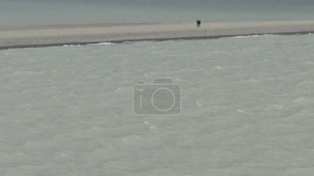 Paar spaziert in Zeitlupe am Strand zwischen eisigem Wasser.
