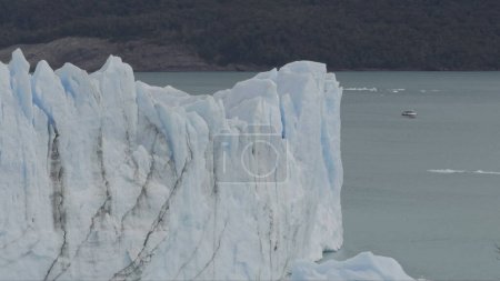 Tour boat approaches Perito Moreno Glaciers high ice cliffs in a remote adventure.