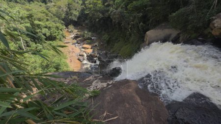 Vidéo aérienne ralentie d'une cascade dans une jungle avec des gens nageant en dessous.