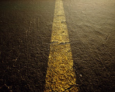 Photo for Worn out and cracked old asphalt of a highway with a yellow divide line. Detail shot. - Royalty Free Image