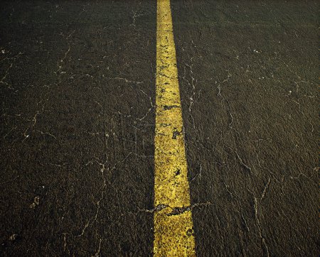 Photo for Worn out and cracked old asphalt of a highway with a yellow divide line. Detail shot. - Royalty Free Image