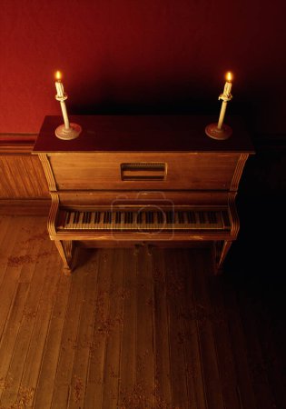 Photo for Vintage rustic interior with vintage piano with candles on it on wooden floor against red wallpaper with wooden paneling. - Royalty Free Image