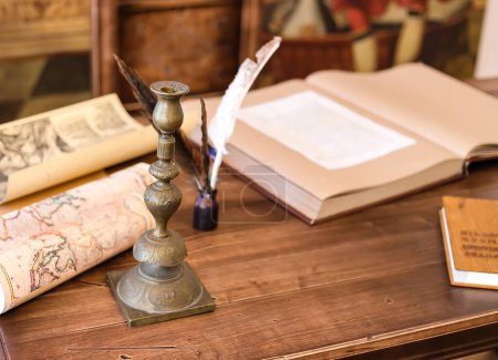 Téléchargez les photos : Ancien chandelier en bronze sur une table en bois avec un livre ouvert et des cartes géographiques anciennes en arrière-plan - en image libre de droit