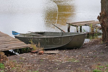 Photo for A metal boat with oars on the shore of the lake. Fisherman's boat. - Royalty Free Image