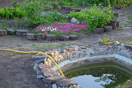 Landscaping. The garden pond fills with water. Flowerbed with flowers.