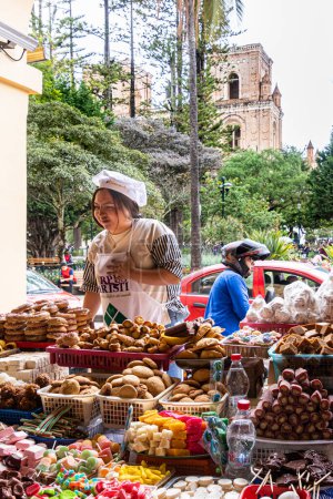 Téléchargez les photos : Cuenca, Équateur-13 juin 2023 : Femme vend des bonbons de différentes saveurs, formes, couleurs lors de la célébration catholique du Corpus Christi. Cathédrale de la Inmaculada Concepcin de Cuenca est en arrière-plan - en image libre de droit