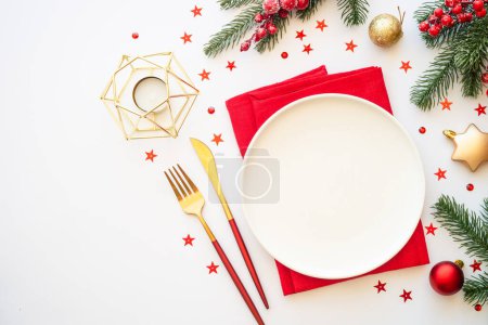 Foto de Ajuste de mesa de Navidad con plato, cubiertos y decoraciones navideñas sobre fondo blanco. Imagen plana con espacio de copia. - Imagen libre de derechos
