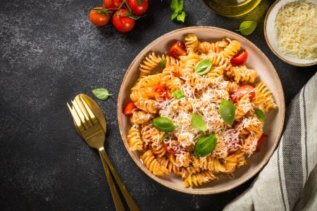 Italienische Pasta alla arrabiata mit frischen Tomaten, Basilikum und Parmesan auf schwarzem Steintisch. Wohnung lag mit Kopierraum.