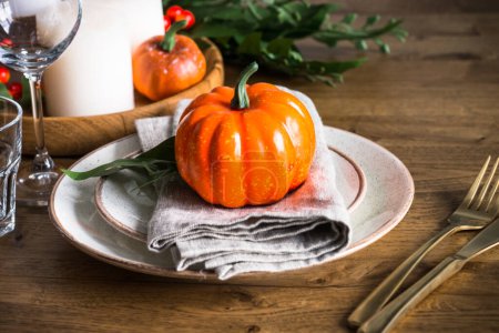 Table setting with plate, pumpkin and candles at wooden table. Autumn table decorations. Thanksgiving food, dinner concept.