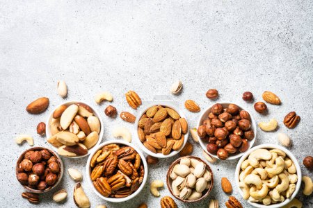 Photo for Assortment of nuts in the bowls. Cashew, hazelnuts, pecan, almonds, brazilian nuts and pistachios at light stone table. Top view with copy space. - Royalty Free Image