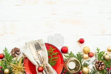 Foto de Ajuste de mesa de Navidad con platos artesanales, cubiertos, velas y decoraciones navideñas sobre fondo de madera blanca. Vista superior con espacio para texto. - Imagen libre de derechos