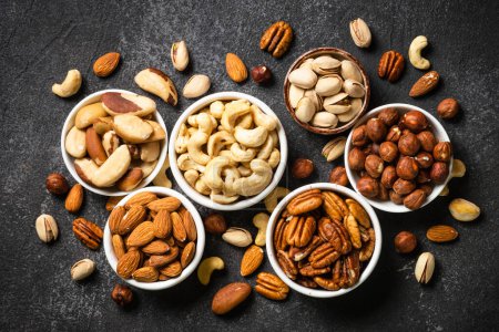 Photo for Assortment of nuts in bowls. Cashew, hazelnuts, pecan, almonds, brazilian nuts and pistachios. Top view with at black stone table. - Royalty Free Image