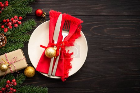 Photo for Christmas table setting with craft plate, cutlery, gift box and christmas decorations on dark wooden background. Top view with copy space. - Royalty Free Image