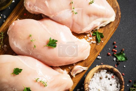 Téléchargez les photos : Poitrine de poulet avec des épices sur fond noir. Viande crue fraîche. Vue supérieure avec espace de copie. - en image libre de droit