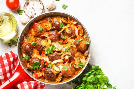 Photo for Meatballs with mushrooms in tomato sauce in a frying pan at light stone table. Top view with copy space. - Royalty Free Image
