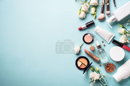 Make up professional cosmetics on blue background. Cream, powder, shadow, brushes with green leaves and flowers. Flat lay image with copy space.