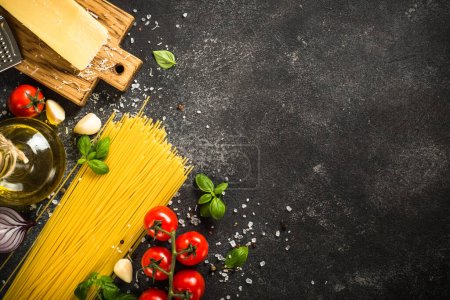 Italienische Lebensmittel Hintergrund schwarzer Tisch. Rohe Nudeln, frische Tomaten, Olivenöl, Parmesan, Gewürze und Basilikum. Draufsicht mit Kopierraum.