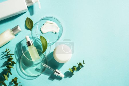 Photo for Cosmetic laboratory concept . Glass petri dish with cosmetic products and serum bottles at blue background. Flat lay image with copy space. - Royalty Free Image