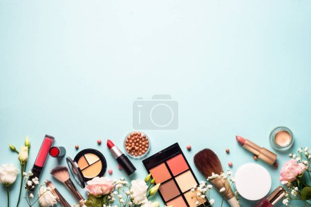 Téléchargez les photos : Make up professional cosmetics on blue background. Cream, powder, shadow, brushes with green leaves and flowers. Flat lay image with copy space. - en image libre de droit