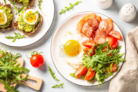 Foto de Healthy breakfast or lunch. Beacon, eggs, toast with avocado and fresh salad. Top view on white. - Imagen libre de derechos