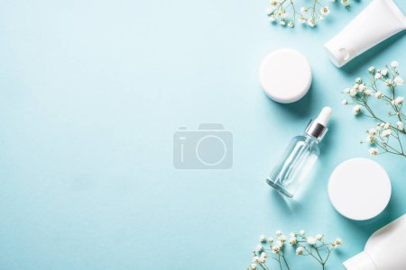 Foto de Natural cosmetic products at blue background. Cream, serum, tonic with green leaves and flowers. Flat lay image with copy space. - Imagen libre de derechos