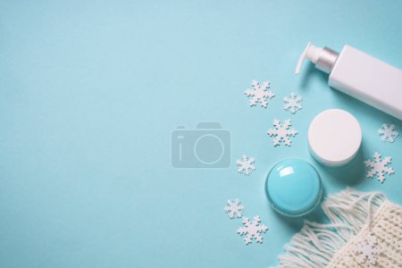 Téléchargez les photos : Cosmétique d'hiver avec foulard tricoté sur fond bleu. Pose plate avec espace de copie. - en image libre de droit