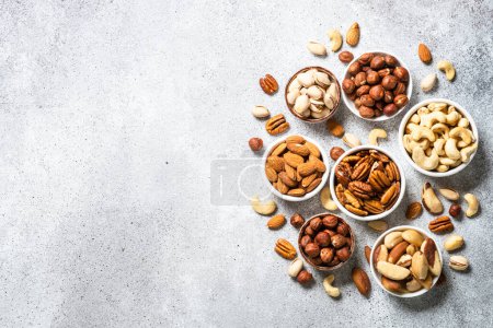 Photo for Assortment of nuts in bowls. Cashew, hazelnuts, pecan, almonds, brazilian nuts and pistachios at light table. Top view with copy space. - Royalty Free Image