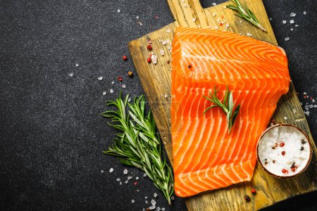 Téléchargez les photos : Filet de saumon cru avec des ingrédients pour cuisiner sur fond noir. Vue de dessus. Prêt pour la cuisson. - en image libre de droit