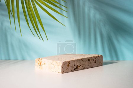 Foto de Podio de piedra para la presentación de productos cosméticos sobre fondo azul con hojas de palma. - Imagen libre de derechos