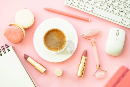 Foto de Espacio de trabajo de oficina creativa. Fondo plano rosa con teclado, taza de café, macarrones y cosméticos. - Imagen libre de derechos