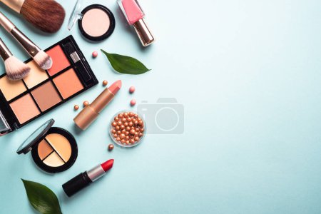 Téléchargez les photos : Make up professional cosmetics on blue background. Powder, lipstick, shadow, brushes with green leaves. Flat lay with copy space. - en image libre de droit