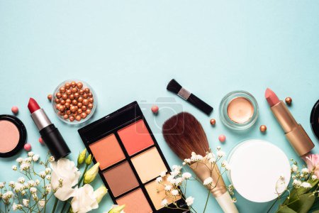 Foto de Make up professional, Cosmetic products on blue background. Cream, powder, shadow, brushes with green leaves and flowers. Top view with copy space. - Imagen libre de derechos
