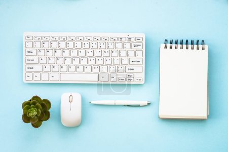 Foto de Escritorio de oficina de fondo plano con teclado, bloc de notas, planta verde, ratón y pluma. - Imagen libre de derechos