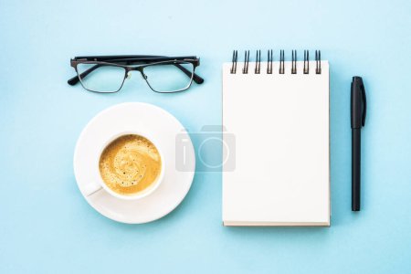Téléchargez les photos : Office desk with notepad, pen, glasses and cup of coffee. Flat lay on blue with copy space. - en image libre de droit