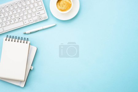 Foto de Escritorio de mesa de oficina con laptop, bloc de notas, bolígrafo y taza de café. Piso puesto en azul con espacio de copia. - Imagen libre de derechos