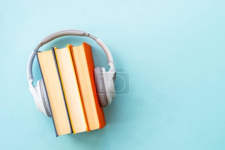 Foto de Concepto de audiolibros. Auriculares y libros sobre fondo azul. Escucha, estudio, podcast. - Imagen libre de derechos