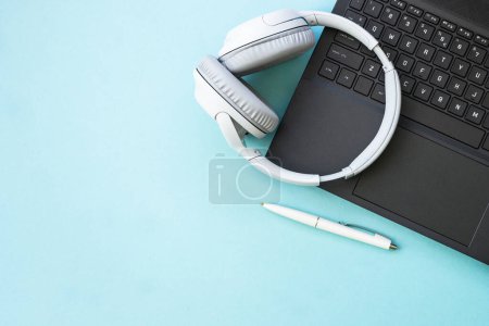 Téléchargez les photos : Laptop and wireless headphones on blue background. Flat lay with copy space. Podcast, listening, studying, music concept. - en image libre de droit