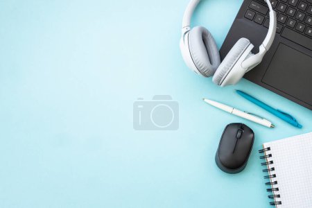Foto de Office desk with laptop, headphones, notepad and pen. Flat lay image on blue with copy space. - Imagen libre de derechos