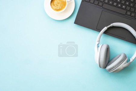 Foto de Office desk with laptop, headphones, notepad and pen. Flat lay image on blue with copy space. - Imagen libre de derechos