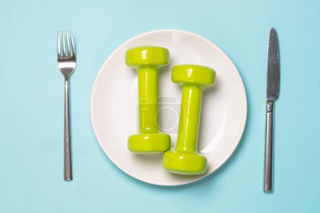 Photo for Dumbbells, white plate and utensil on blue. Healthy lifestile, fitness, diet and weight loss concept. - Royalty Free Image