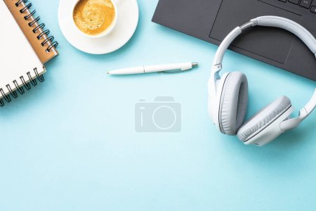 Téléchargez les photos : Office workspace with laptop, headphones, notepad and coffee cup. Flat lay image on blue with copy space. - en image libre de droit