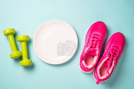 Téléchargez les photos : Dumbbells, white plate and sport shoes on blue. Healthy lifestile, fitness, diet and weight loss concept. - en image libre de droit