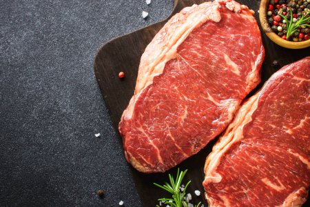 Foto de Raw beef meat. Fresh meat steaks at black board. Top view. - Imagen libre de derechos