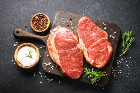 Foto de Raw beef meat. Fresh meat steaks at black board. Top view. - Imagen libre de derechos