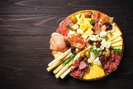Photo for Antipasto at wooden serving board. Cheese and meat - jamon, salami with olives at wooden table. Top view with copy space. - Royalty Free Image