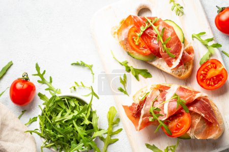 Téléchargez les photos : Open sandwiches with cream cheese, prosciutto and arugula at white background. Flat lay image. - en image libre de droit