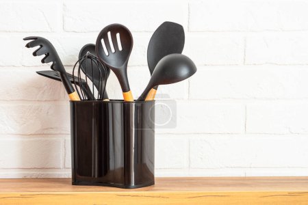 Téléchargez les photos : Kitchen utensils, cooking tools in black container near white wall. - en image libre de droit