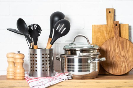 Foto de Kitchen utensils. Cooking tools with cooking pots, wooden cutting boards at white modern kitchen interior. - Imagen libre de derechos
