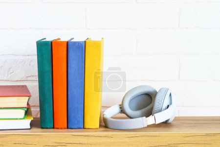 Foto de Audio books concept. Wireless Headphones and color books at wooden table white background. - Imagen libre de derechos