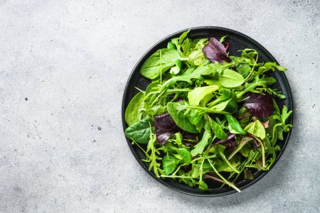 Téléchargez les photos : Green salad with fresh leaves in black plate. Healthy food, clean eating, diet. Top view. - en image libre de droit